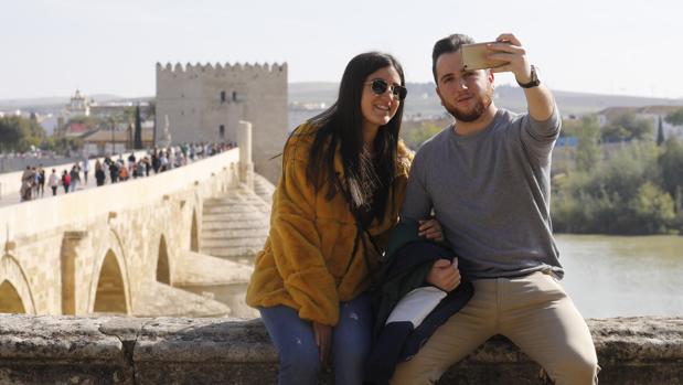 Una pareja de jóvenes turistas se fotografía con el Puente Romano y la Torre de la Calahorra al fondo