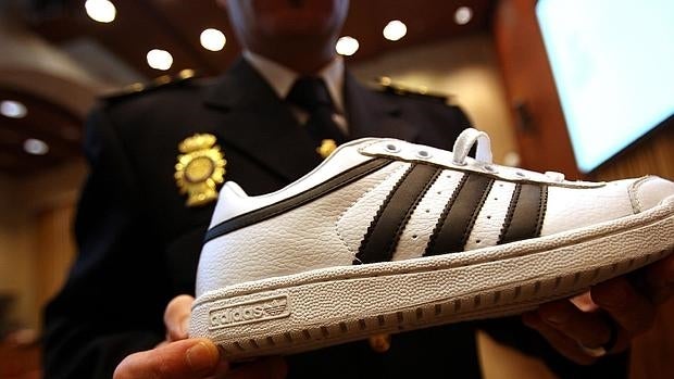 Un policía muestra una zapatilla falsa después de que la Asociación Nacional para la Defensa de la Marca y la Policía Nacional informara del proceso que ha llevado a un juez a impedir el acceso desde España, de forma cautelar, a una página electrónica de venta de productos falsificados