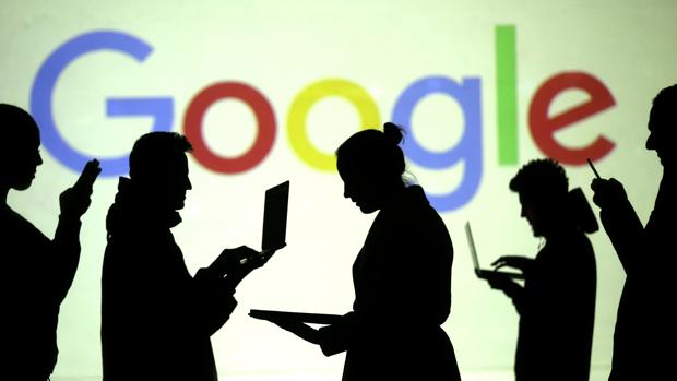Un grupo de personas utilizando ordenadores y móviles delante de una pantalla de Google