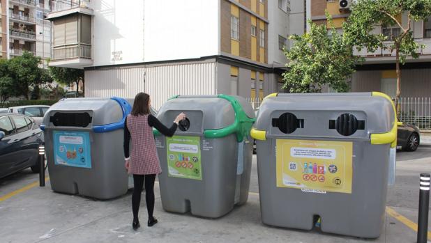 Una joven deposita una botella de vidrio en un contenedor verde de Lipasam