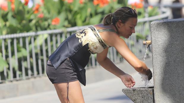 Una mujer se refresca en una fuente de Sevilla
